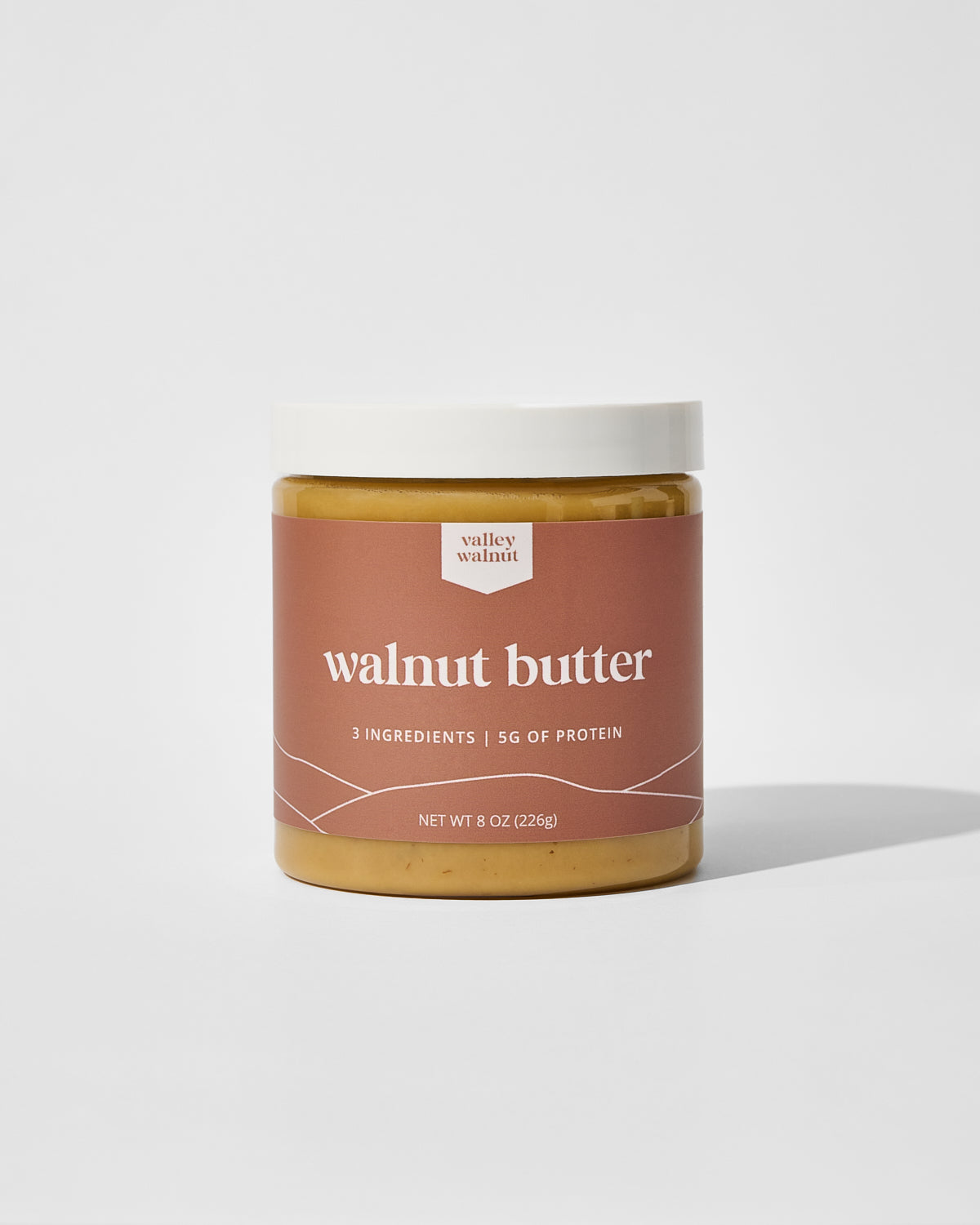 A jar of Valley Walnut walnut butter with a white lid and a dusty rose label, set against a clean white background with a soft shadow.
