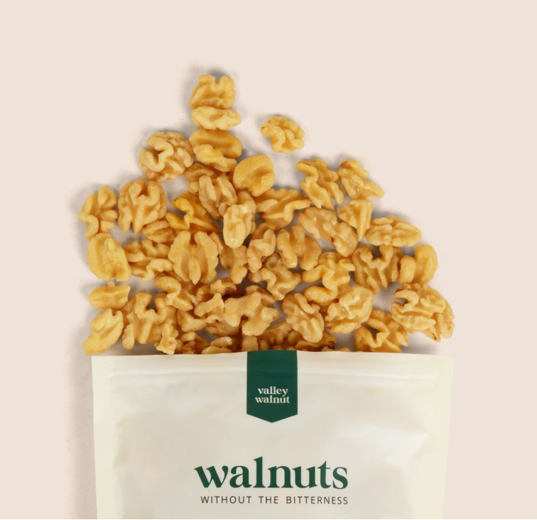Valley Walnut packaging with walnuts spilling out on a beige background